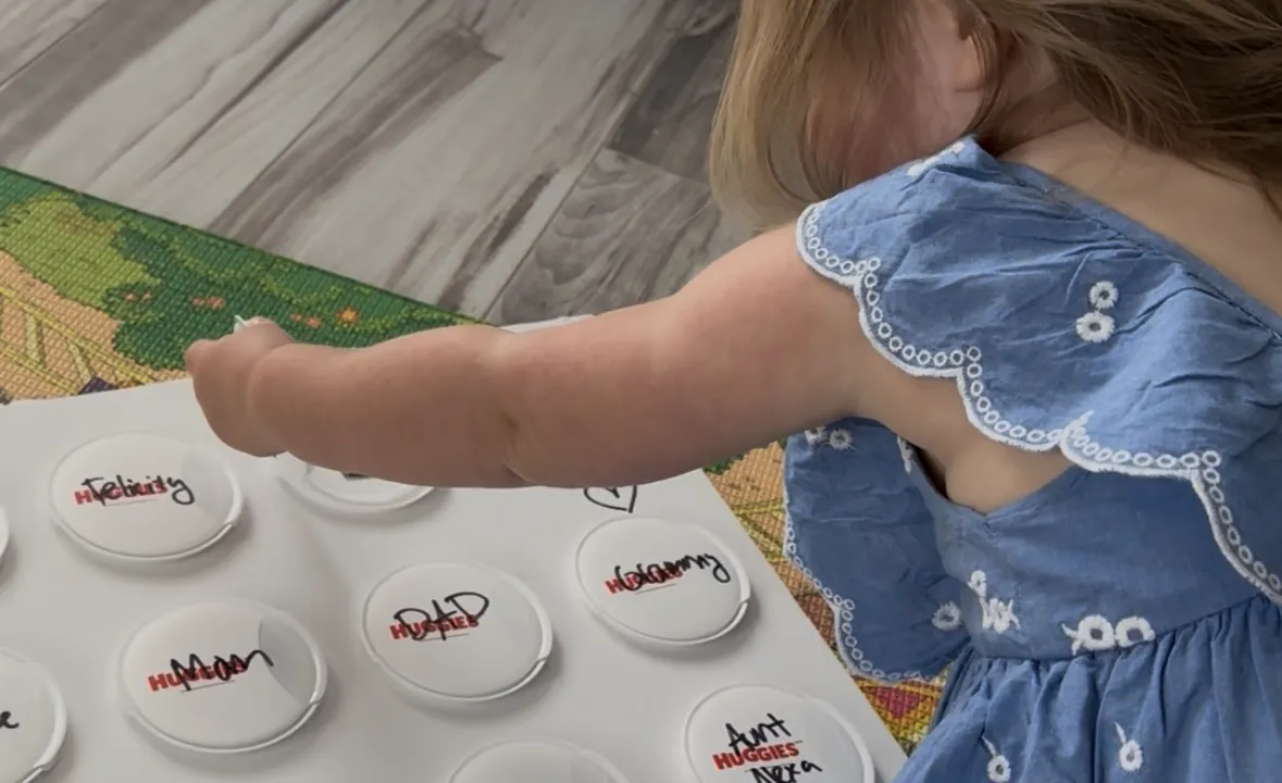 Toddler lifting a baby wipe lid on a cardboard board to reveal a family photo underneath