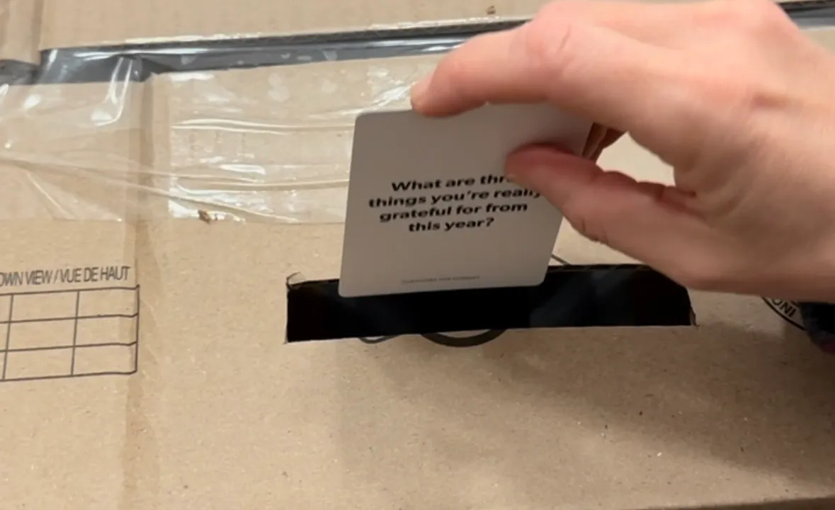 Toddler pushing a playing card through a slit cut into the top of a cardboard box