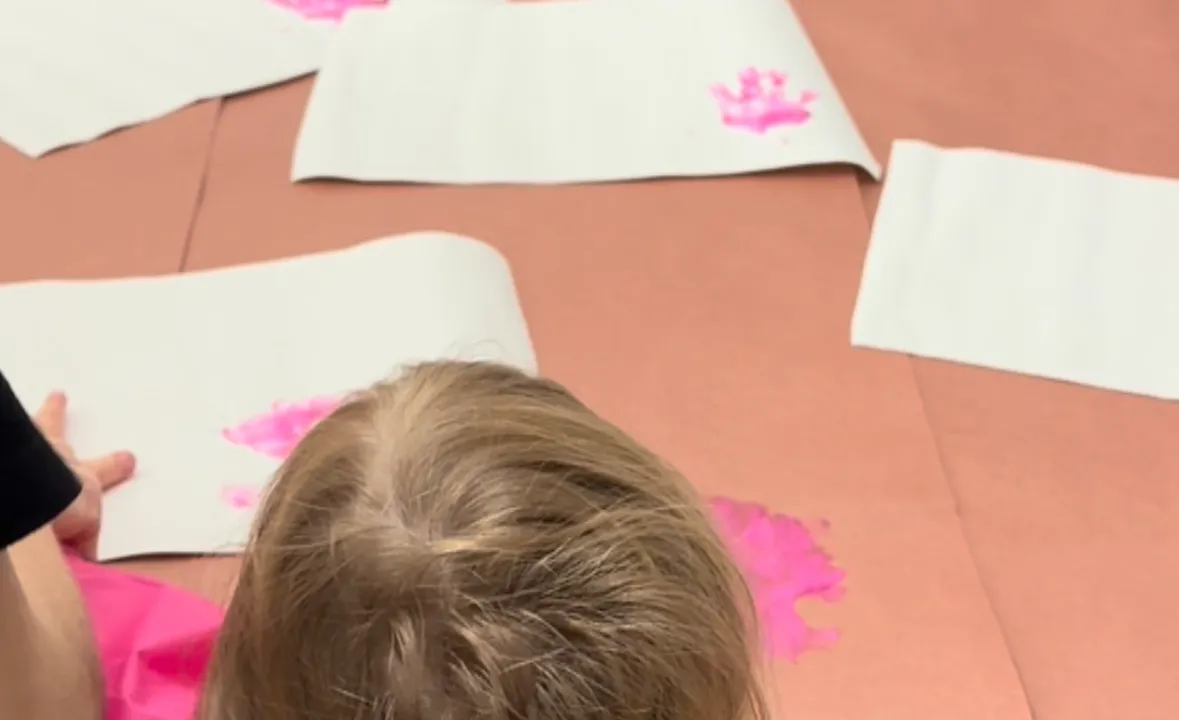 Toddler with blue and pink paint on her palms pressing hand prints onto a sheet of white card stock