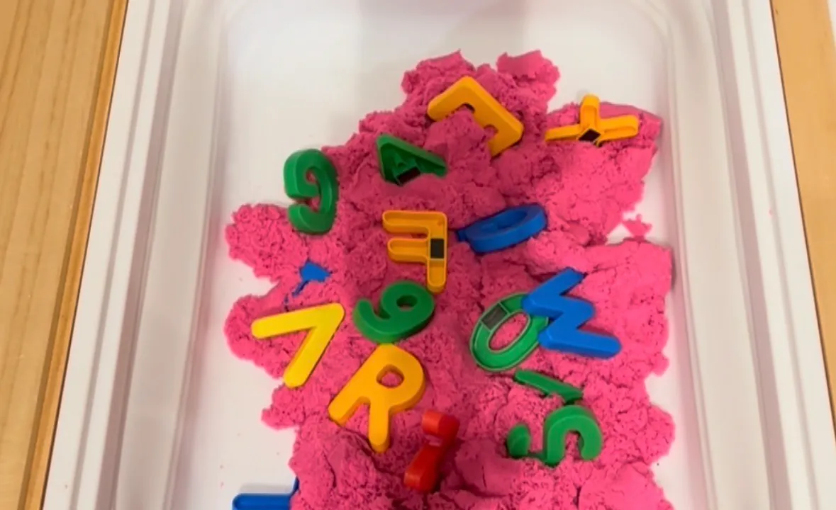 Toddler digging small hidden toys out of a tray of beige kinetic sand