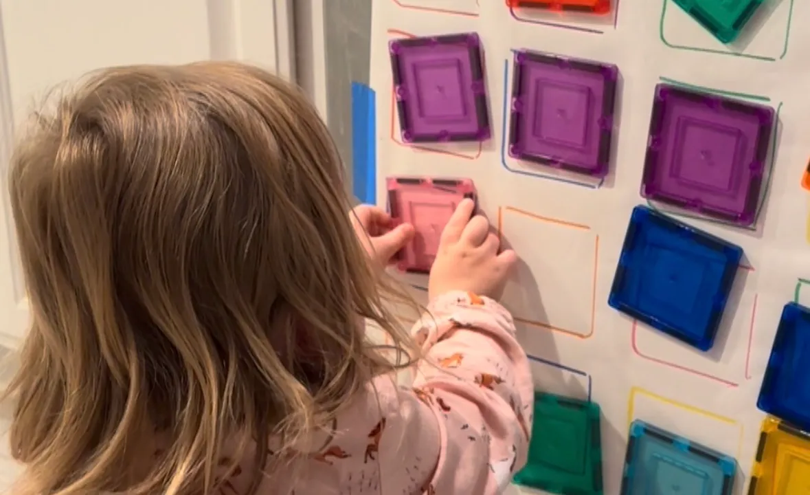 Toddler pressing colored magnetic tiles onto matching colored squares taped to a dishwasher front