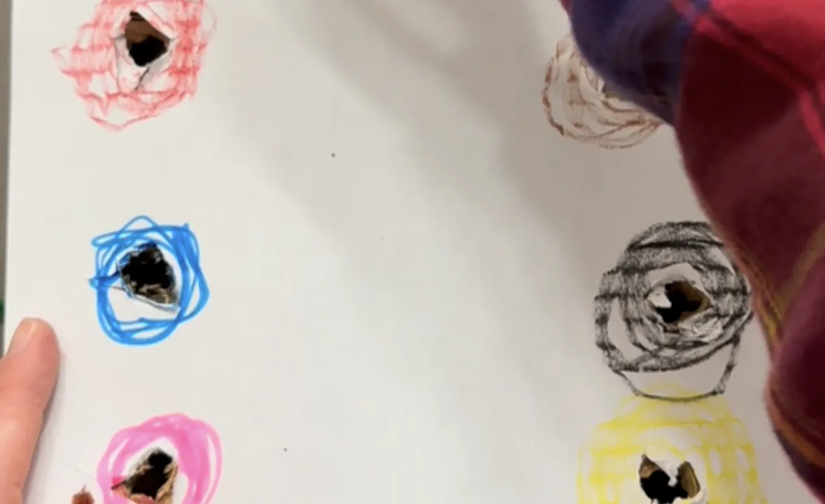 Toddler poking a colored pipe cleaner into a matching colored hole on the side of a cardboard box